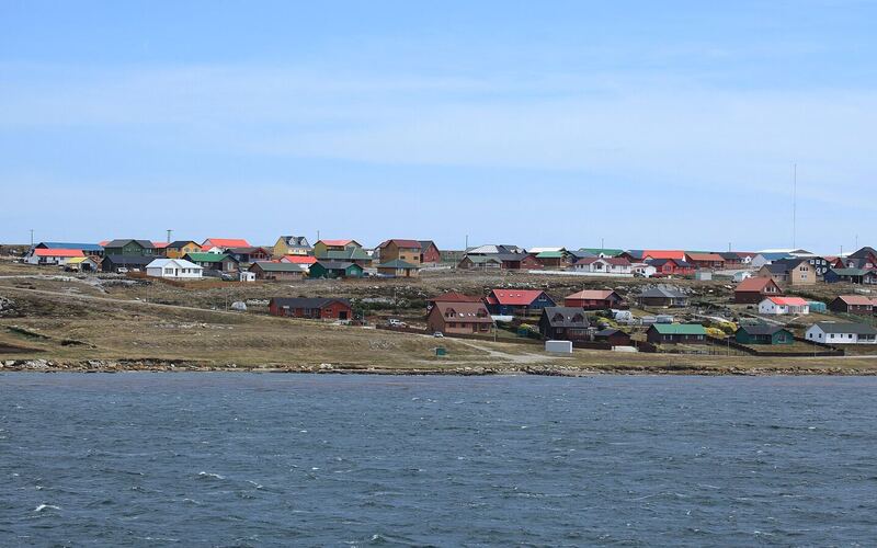Gekleurde huizen van Stanley aan de overkant van het water van Stanley Harbour onder een blauwe lucht