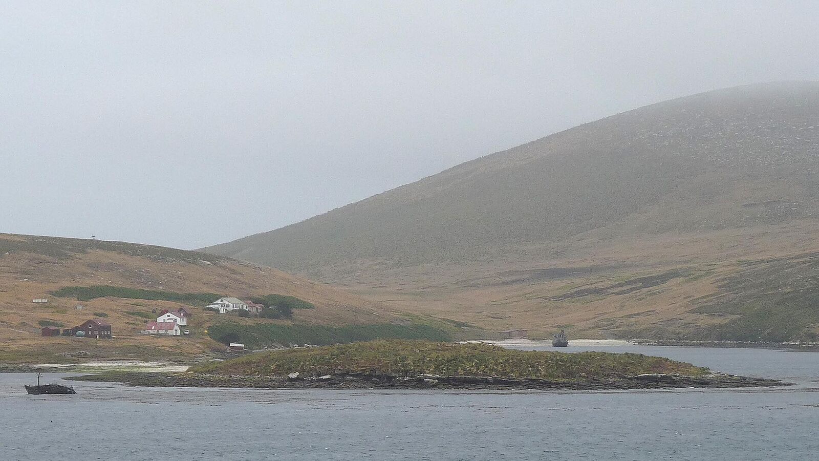 De kleine settlement van New Island aan Coffin's Harbour met heuvels en een scheepswrak in de baai