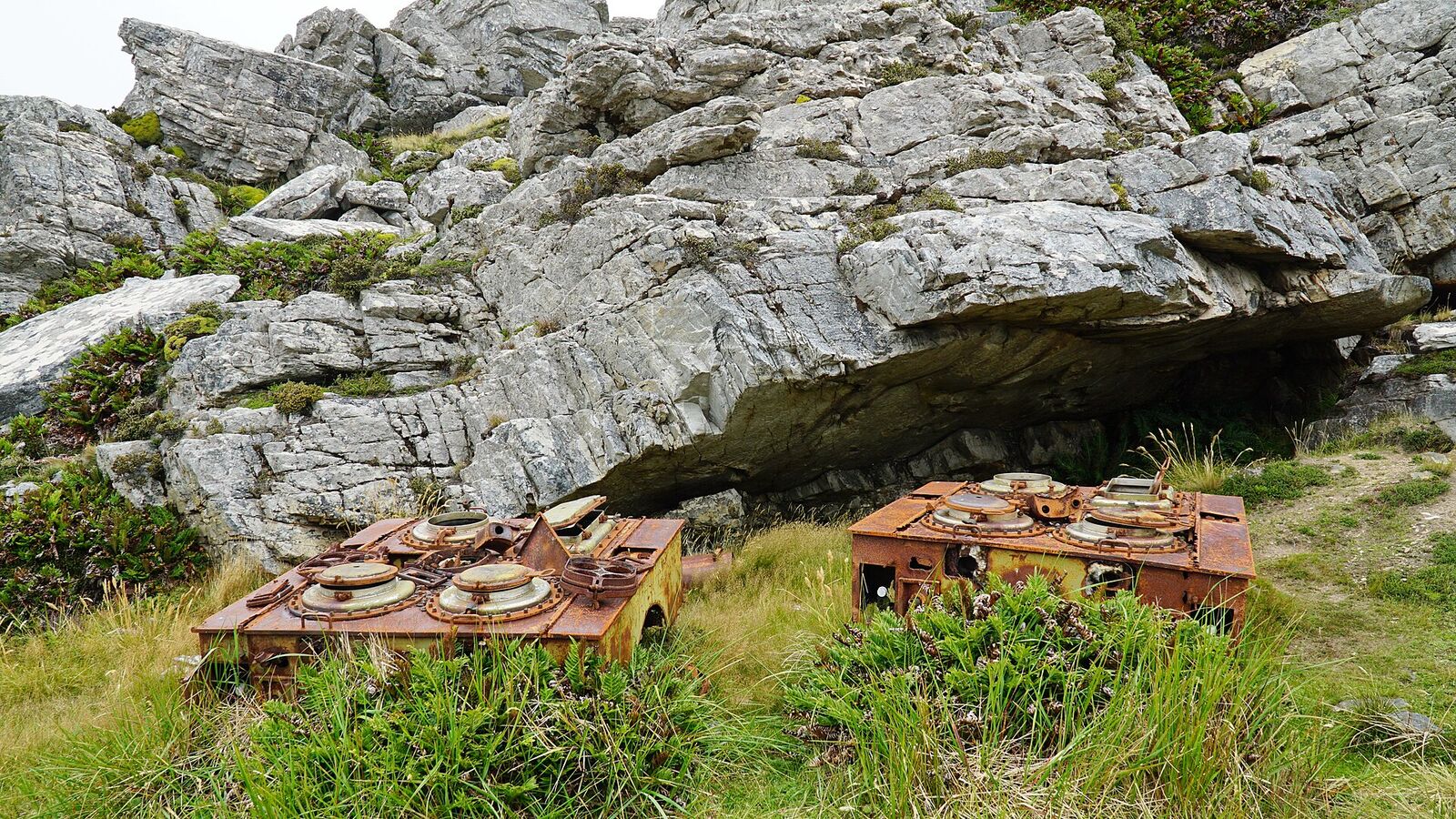 Twee verroeste kookketels van een Argentijnse veldkeuken uit 1982 in het gras onder een rotswand op Mount Tumbledown