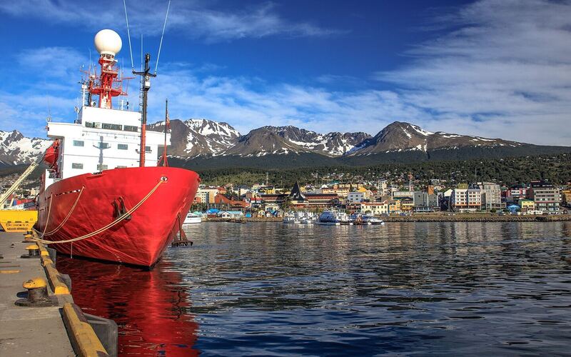 Rood-wit onderzoeksschip aan de kade van Ushuaia, met de stad en besneeuwde bergen op de achtergrond