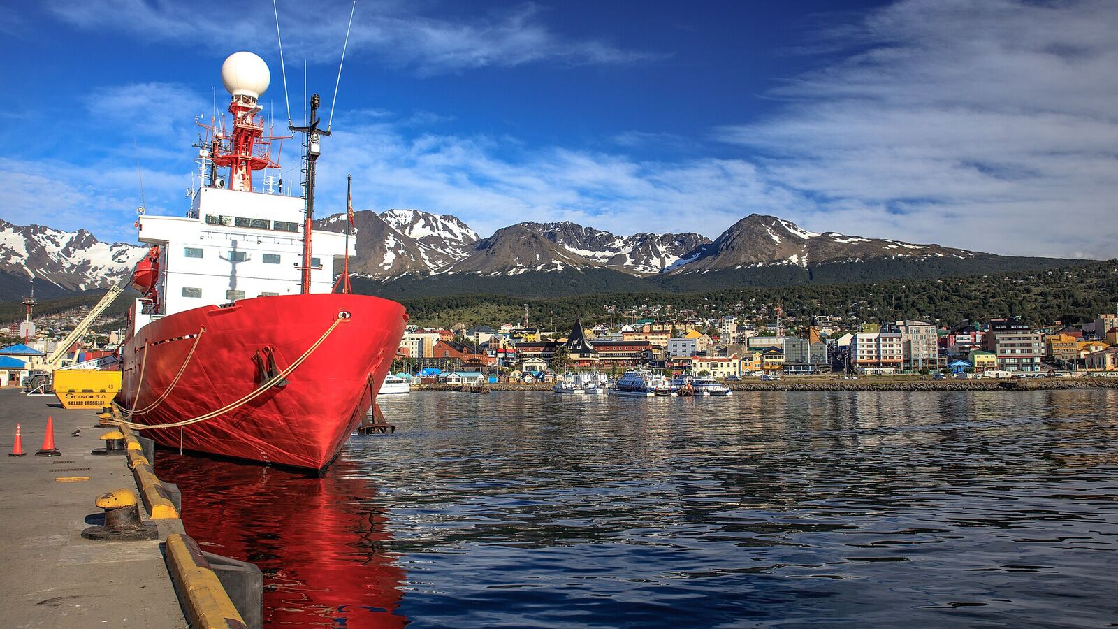 Rood-wit onderzoeksschip aan de kade van Ushuaia, met de stad en besneeuwde bergen op de achtergrond